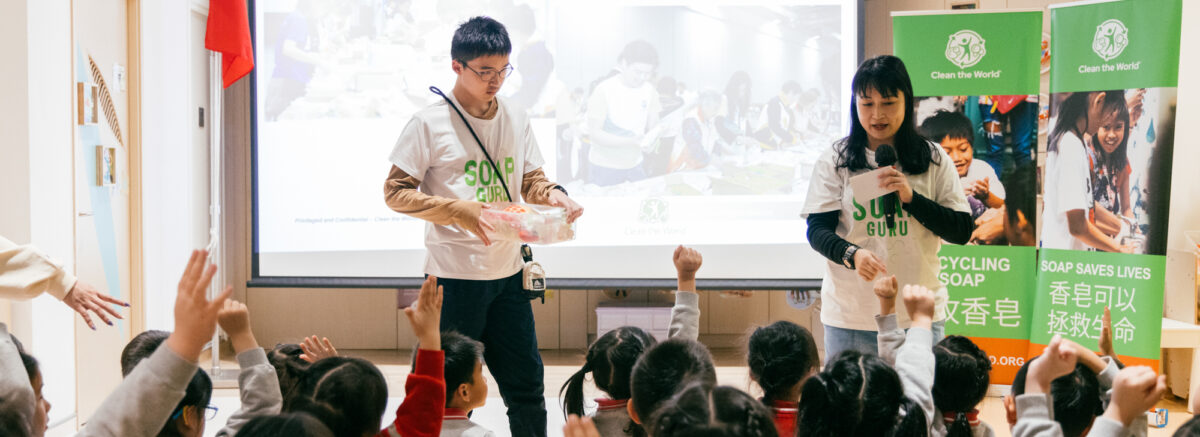 Clean the World Asia - Charity event in Hong Kong at a local kindergarten, with a female speaker and young kids raising hands