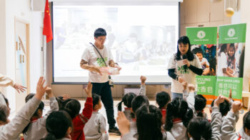 Clean the World Asia - Charity event in Hong Kong at a local kindergarten, with a female speaker and young kids raising hands